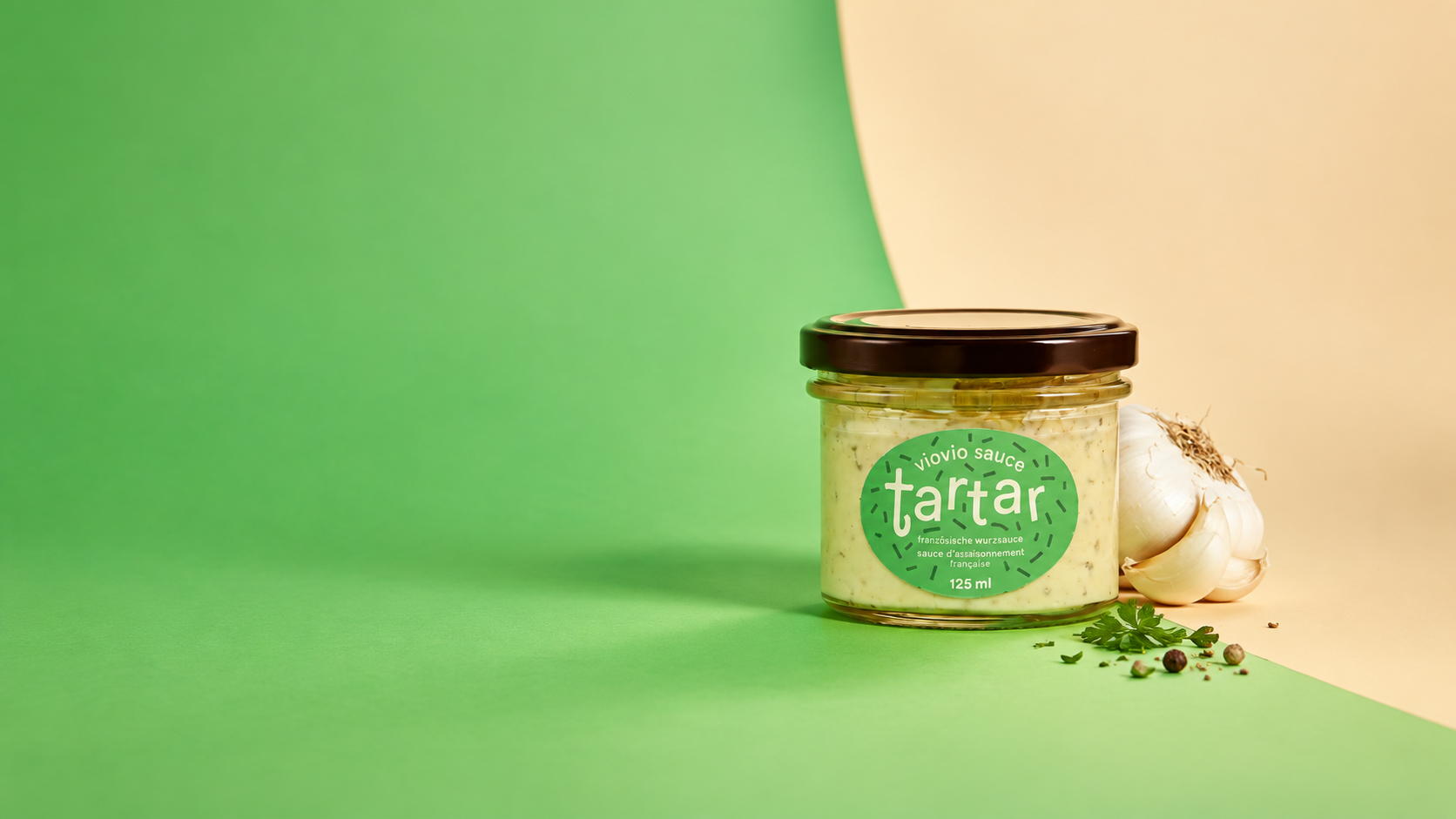 Sturzglas von Müller+Krempel mit Twist-off-Deckel, befüllt mit Tartarsauce und dekoriert mit Knoblauch, vor grün-beigem Hintergrund.
